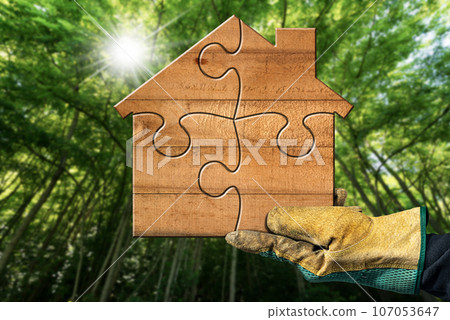 Gloved Hand Holding a Small Wooden House Made of Puzzle Pieces 107053647