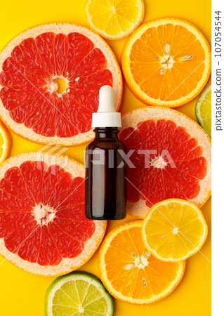 Citrus essential oil bottle on yellow background with sliced citrus fruits top view 107054544