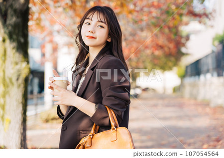 A woman drinking coffee with autumn leaves in the background A woman drinking coffee with autumn leaves in the background 107054564