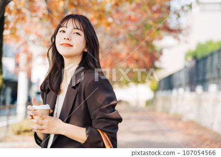 A woman drinking coffee with autumn leaves in the background A woman drinking coffee with autumn leaves in the background 107054566