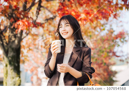 A woman drinking coffee with autumn leaves in the background 107054568