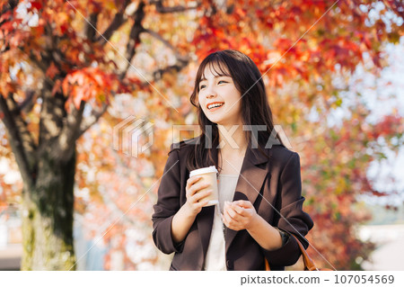 A woman drinking coffee with autumn leaves in the background A woman drinking coffee with autumn leaves in the background 107054569