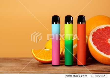 Three electronic cigarettes with citrus fruits on orange background Three electronic cigarettes with citrus fruits on orange background 107054640
