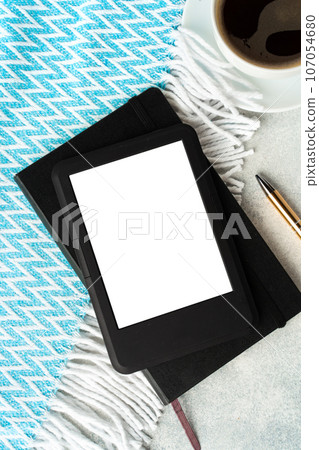 Composition with modern e-book reader, hardcover book and cup of coffee on table Composition with modern e-book reader, hardcover book and cup of coffee on table 107054680