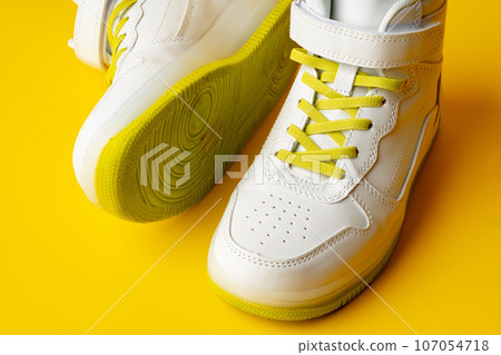 White sneakers with yellow neon laces on yellow background White sneakers with yellow neon laces on yellow background 107054718