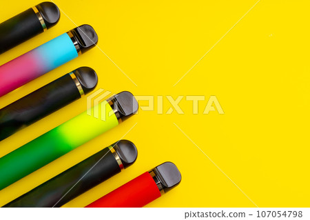 Colorful disposable electronic cigarettes on yellow background 107054798