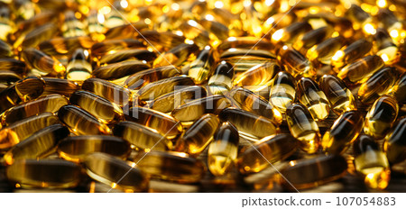 Many yellow Vitamin D, Fish Oil, Omega-3 capsules in sunshine light on table. Soft Fish Oil, Vitamin D supplements capsules on wooden background. Selective focus Many yellow Vitamin D, Fish Oil, Omega-3 capsules in sunshine light on table. Soft Fish Oil, Vitamin D supplements capsules on wooden background. Selective focus 107054883