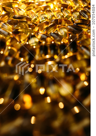 Many yellow Vitamin D, Fish Oil, Omega-3 capsules in sunshine light on table. Soft Fish Oil, Vitamin D supplements capsules on wooden background. Selective focus Many yellow Vitamin D, Fish Oil, Omega-3 capsules in sunshine light on table. Soft Fish Oil, Vitamin D supplements capsules on wooden background. Selective focus 107054884