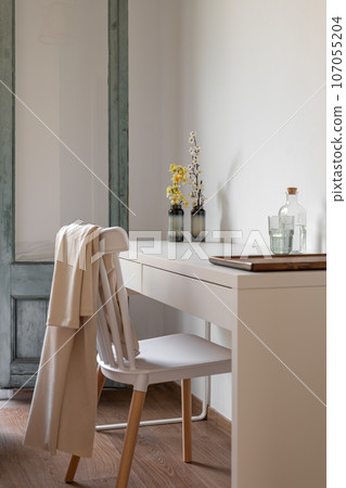 Vertical shot chair stands behind a table in a living room for single travelers with decor and water. High class service hotel concept. Copyspace Vertical shot chair stands behind a table in a living room for single travelers with decor and water. High class service hotel concept. Copyspace 107055204