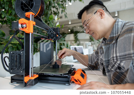 Asian designer engineer using 3D printer in laboratory and studying product prototype. 107055448