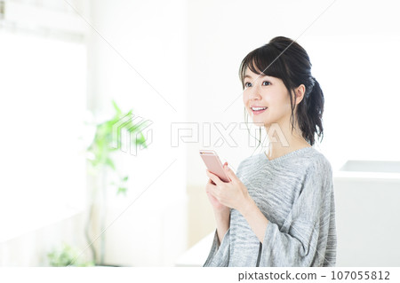 一個年輕的女人，在客廳裡操作智能手機 107055812