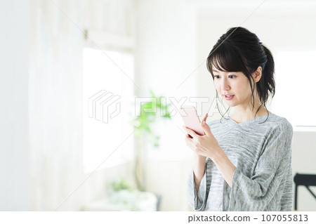 一個年輕的女人，在客廳裡操作智能手機 107055813