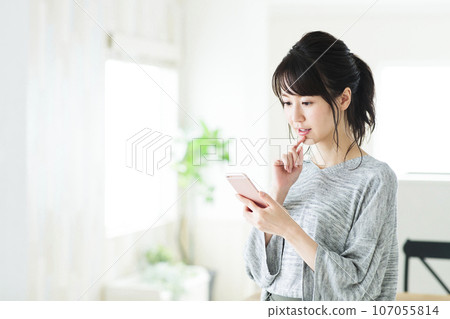 一個年輕的女人，在客廳裡操作智能手機 107055814