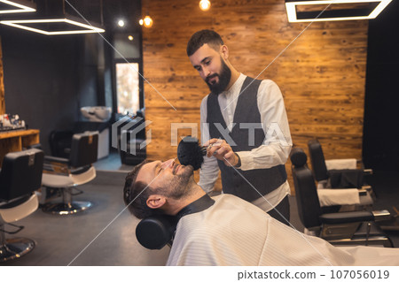 Caucasian man getting perfect shape of beard at barbershop. 107056019