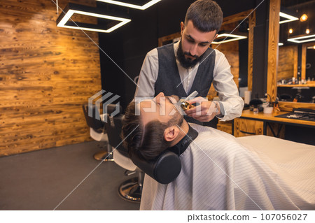 Bearded man getting beard haircut by hairdresser at barbershop. Bearded man getting beard haircut by hairdresser at barbershop. 107056027