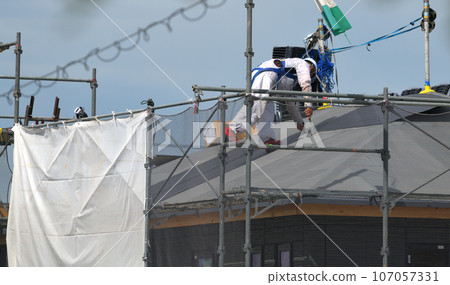Workers working at a construction site. Work scene of a roofer working on a newly built detached house. 107057331