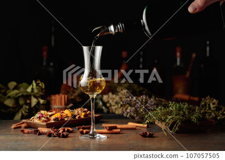 Yellow herbal liquor or balm is poured from a vintage bottle into a glass. Yellow herbal liquor or balm is poured from a vintage bottle into a glass. 107057505