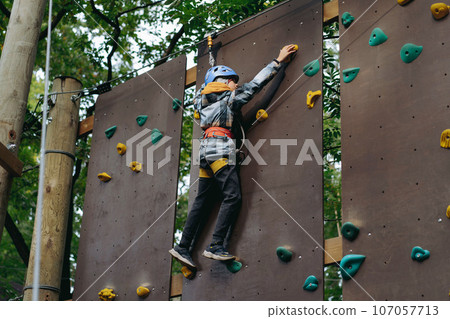 teenage boy climbing up the wall in outdoor adventure park passing obstacle course. high rope park 107057713