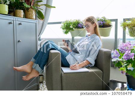 Student girl studying at home, sitting at home in an armchair, using digital tablet 107058479