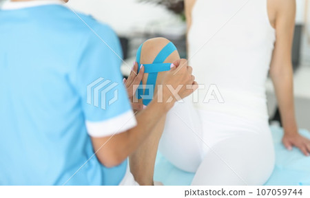 Doctor fixes kinesio tape on patient's leg 107059744