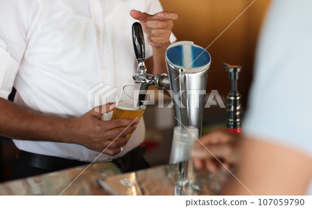 Bartender at bar pours beer into glass 107059790