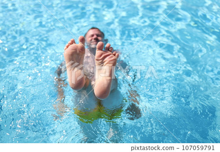 Man shows his feet while lying in pool 107059791