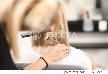 Hairdresser holds comb and scissors in his hands and cuts client's hair 107059799