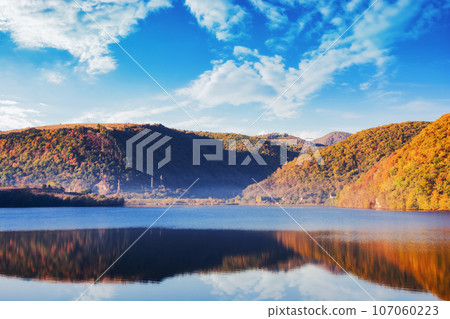 mountainous countryside landscape with lake in autumn. scenery in fall colors. bright sunny weather with clouds on the sky. cluj county, romania 107060223