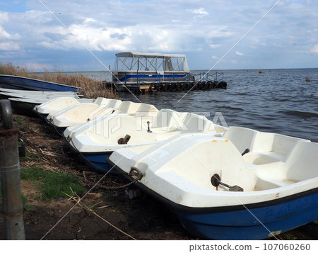 Spring landscape with catamaran and water bikes on the shore of a large lake, against a clear sky. Rural landscape, a beautiful place to relax. Spring landscape with catamaran and water bikes on the shore of a large lake, against a clear sky. Rural landscape, a beautiful place to relax. 107060260