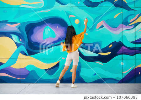 Female street artist painting bright colorful graffiti on wall Female street artist painting bright colorful graffiti on wall 107060385