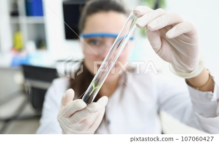 Researcher holds flask with earth and small plant in his hands 107060427
