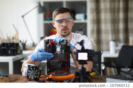 Gloved craftsman holds disassembled computer equipment and shows it to comer 107060512
