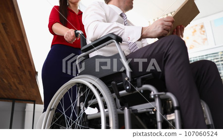 Woman rolls man in a wheelchair in office 107060524