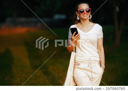 smiling woman in shirt using smartphone app and walking 107060760
