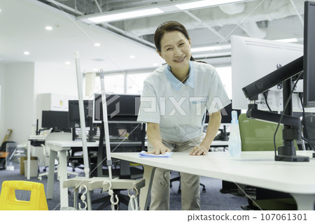 Senior woman wiping down her desk in the office 107061301