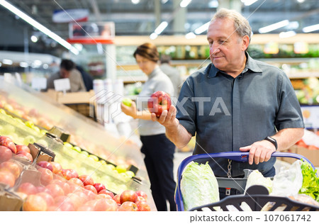 Elderly man chooses apples in vegetable and fruit department 107061742