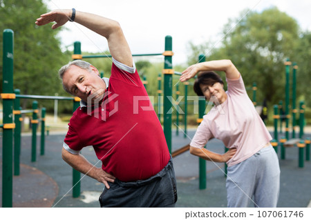 Elderly man and a woman are engaged in gymnastics on an open-air sports ground Elderly man and a woman are engaged in gymnastics on an open-air sports ground 107061746