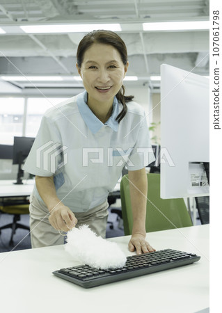 Female cleaning worker removing dust from keyboard in office, vertical position Female cleaning worker removing dust from keyboard in office, vertical position 107061798