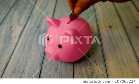 A woman's hand throws coins into a piggy bank A woman's hand throws coins into a piggy bank 107063224