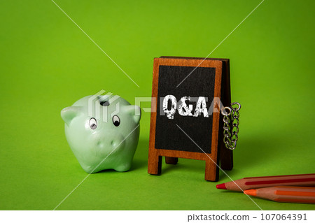 Questions and answers concept. Miniature chalkboard and piggy bank on green background Questions and answers concept. Miniature chalkboard and piggy bank on green background 107064391