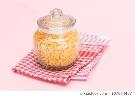Uncooked Chifferi Rigati Pasta in Glass Jar on Checkered Red Towel 107064437
