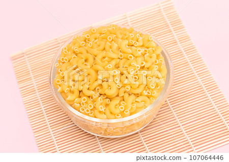 Uncooked Chifferi Rigati Pasta in Glass Jar on Bamboo Mat on Pink Background Uncooked Chifferi Rigati Pasta in Glass Jar on Bamboo Mat on Pink Background 107064446
