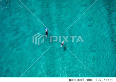 Surfers rowing on surfboards in transparent turquoise ocean waiting wave. Aerial view 107064570
