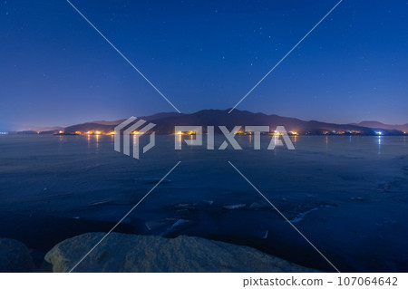 A frozen lake at night in winter with mountains in the background and a sky full of stars at Dumulmeori, Yangpyeong, South Korea. A frozen lake at night in winter with mountains in the background and a sky full of stars at Dumulmeori, Yangpyeong, South Korea. 107064642