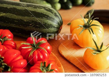 Fresh ripe big tomatoes, eggplant, veggies on a kitchen wooden workplace. Many raw vegetables background. Tomato, cucumbers. Cooker at home making a healthy veggie meal. Preparing vegetarian dish Fresh ripe big tomatoes, eggplant, veggies on a kitchen wooden workplace. Many raw vegetables background. Tomato, cucumbers. Cooker at home making a healthy veggie meal. Preparing vegetarian dish 107065253