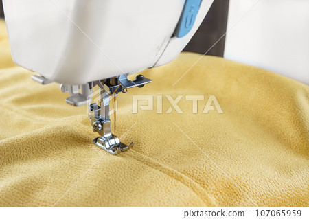 Modern sewing machine with yellow velours fabric close up Modern sewing machine with yellow velours fabric close up 107065959