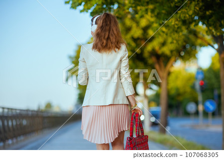 trendy woman in dress and jacket in city listening to music trendy woman in dress and jacket in city listening to music 107068305