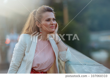 pensive stylish woman in pink dress and white jacket in city 107068310