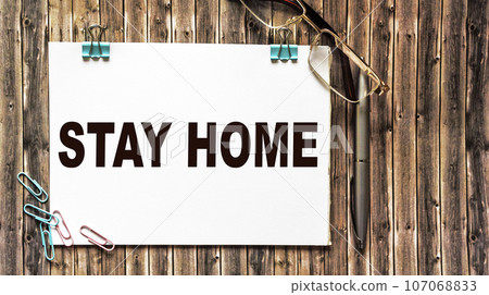 White note with stay at home and paper clips and glasses on wooden background 107068833