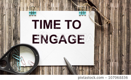 Time to engage , text on notepad, pen, magnifier and glasses on a wooden table. Time to engage , text on notepad, pen, magnifier and glasses on a wooden table. 107068836